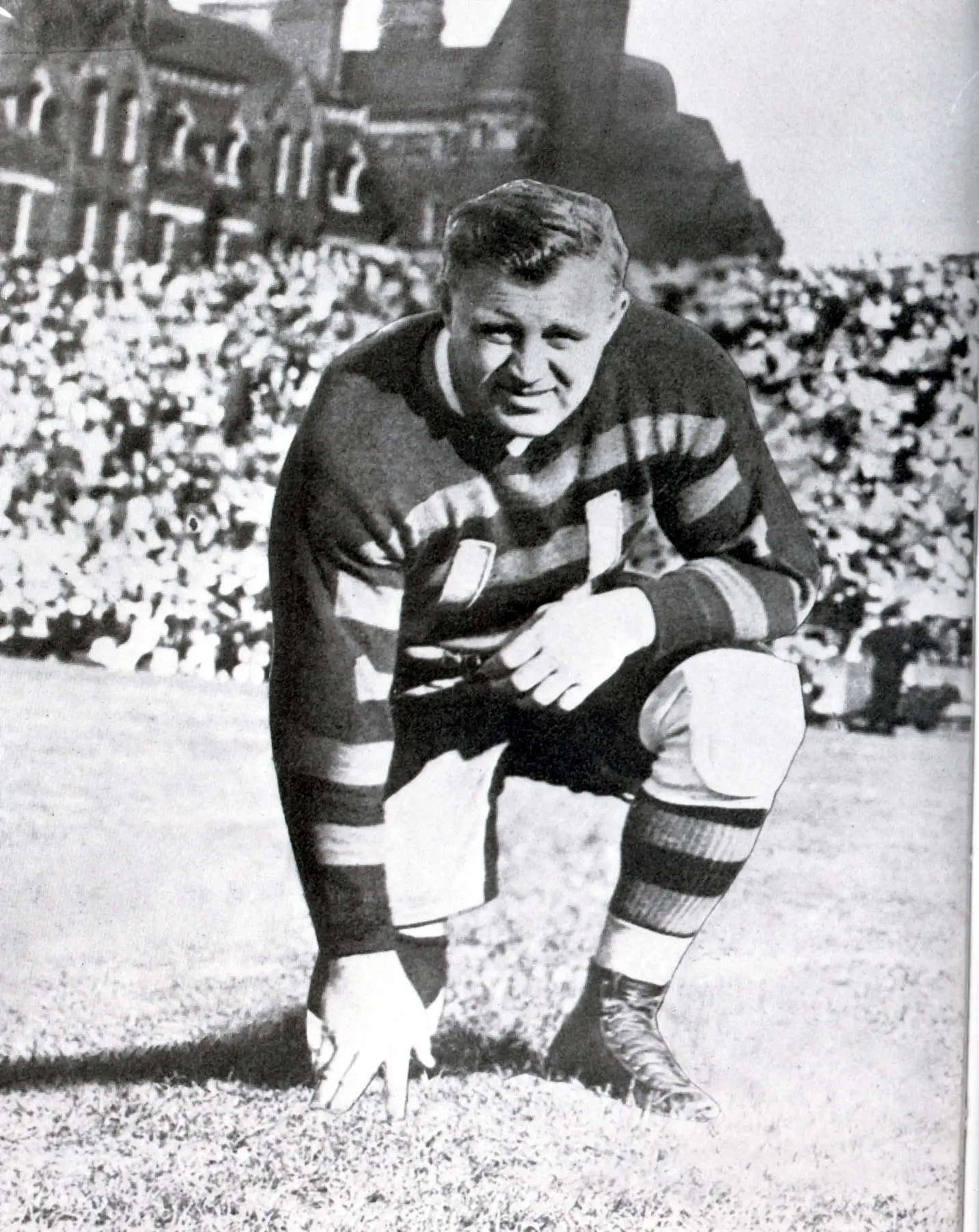 Brian Timmis, kneeling on a football field in sport attire.